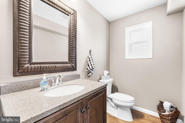 half bath with toilet, baseboards, wood finished floors, and vanity