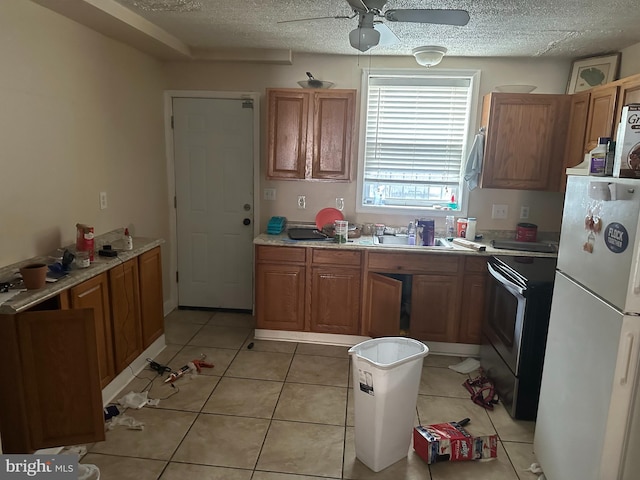 kitchen featuring brown cabinets, light countertops, freestanding refrigerator, a sink, and stainless steel range with electric stovetop