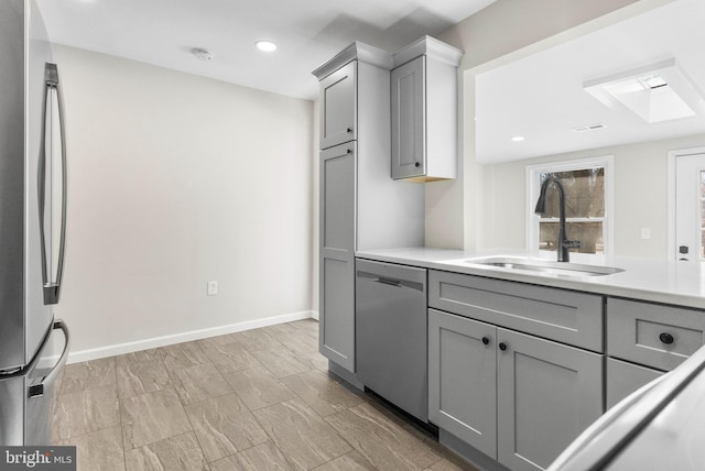 kitchen featuring appliances with stainless steel finishes, light countertops, a sink, and gray cabinetry