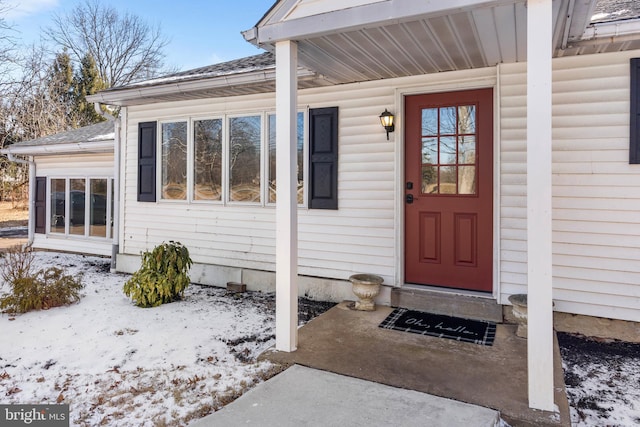 snow covered property entrance featuring a shingled roof