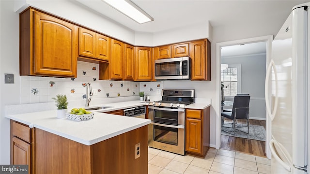 kitchen with stainless steel appliances, brown cabinets, a sink, and backsplash