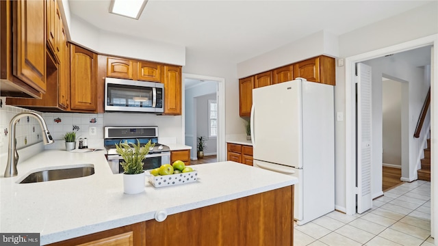 kitchen featuring a peninsula, brown cabinetry, stainless steel appliances, and a sink