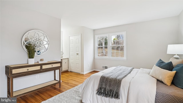 bedroom with light wood-type flooring, visible vents, baseboards, and ensuite bathroom