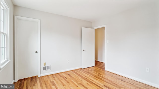 unfurnished bedroom with multiple windows, visible vents, baseboards, and wood finished floors