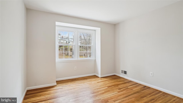 empty room with light wood-type flooring, visible vents, and baseboards