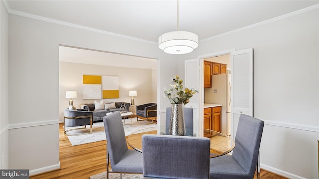 dining area featuring baseboards, crown molding, and light wood finished floors