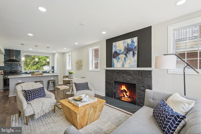 living room featuring baseboards, a stone fireplace, dark wood-style flooring, and recessed lighting