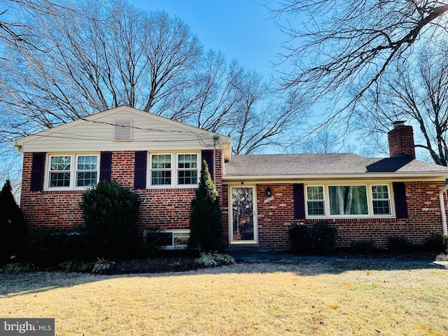 split level home featuring a chimney, a front lawn, and brick siding