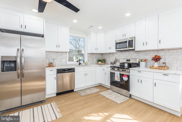 kitchen featuring decorative backsplash, stainless steel appliances, light wood-style floors, white cabinetry, and a sink