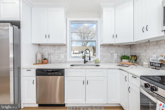 kitchen with white cabinets, light stone counters, stainless steel appliances, and a sink