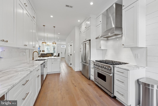 kitchen with visible vents, wall chimney range hood, high quality appliances, and white cabinets