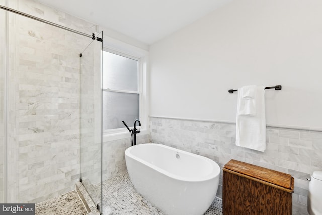 full bath featuring a freestanding tub, wainscoting, a tile shower, and tile walls