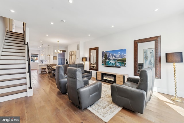 living room with a glass covered fireplace, recessed lighting, light wood finished floors, and stairs