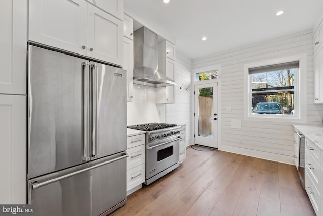 kitchen featuring wall chimney exhaust hood, high quality appliances, white cabinetry, and wood finished floors