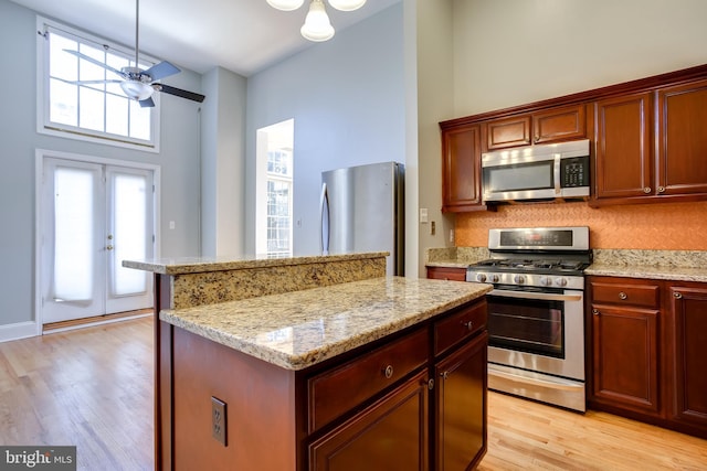 kitchen featuring a center island, stainless steel appliances, light wood-style flooring, ceiling fan, and light stone countertops