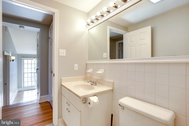 half bath with toilet, wood finished floors, tile walls, vanity, and baseboards