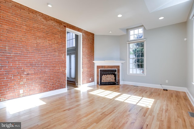 unfurnished living room featuring light wood finished floors, brick wall, and a fireplace