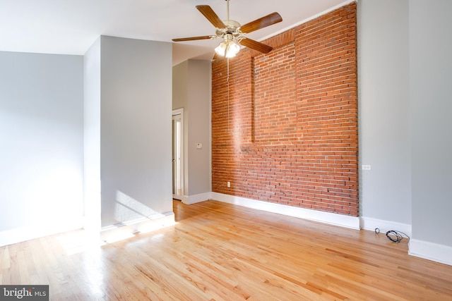 unfurnished room with a high ceiling, brick wall, baseboards, and light wood finished floors