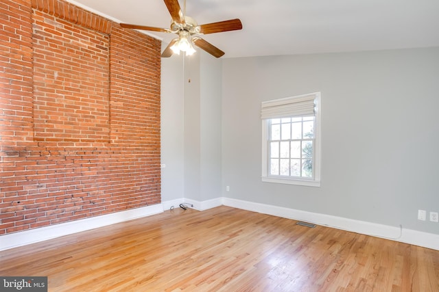 empty room with light wood-style floors, brick wall, visible vents, and baseboards