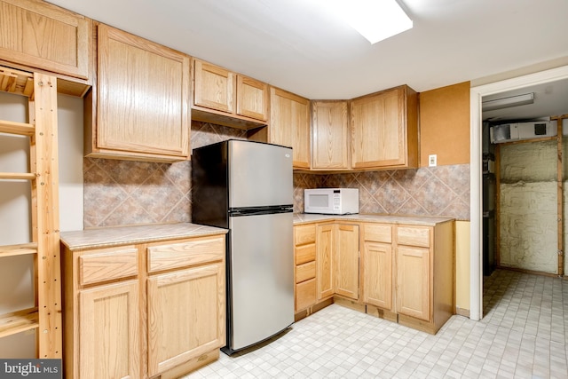 kitchen featuring freestanding refrigerator, light countertops, light brown cabinetry, and white microwave