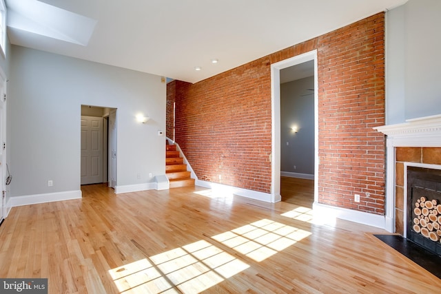 unfurnished living room with baseboards, a tile fireplace, brick wall, stairway, and light wood-style floors