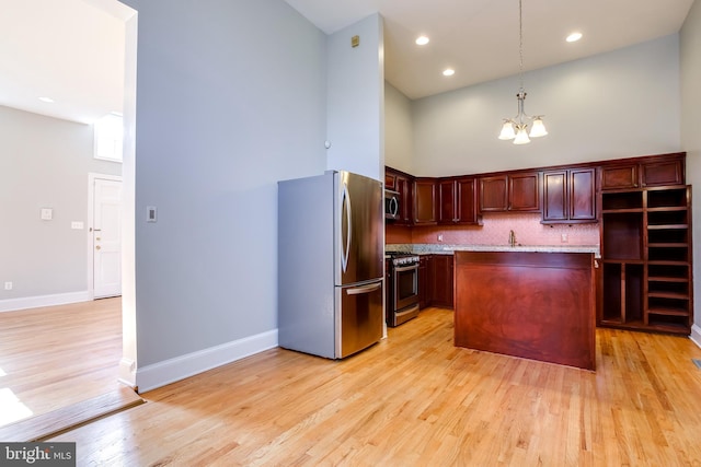 kitchen with light wood-style flooring, a kitchen island, decorative light fixtures, stainless steel appliances, and a notable chandelier