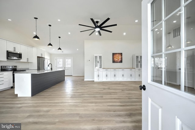 kitchen featuring a center island with sink, stainless steel appliances, light countertops, white cabinetry, and pendant lighting