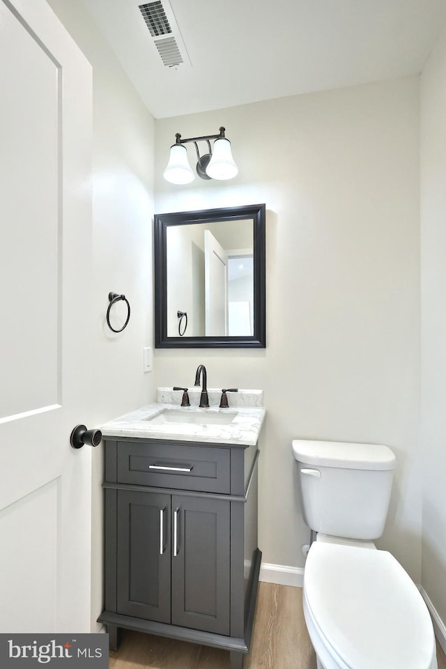 half bathroom featuring toilet, wood finished floors, vanity, visible vents, and baseboards