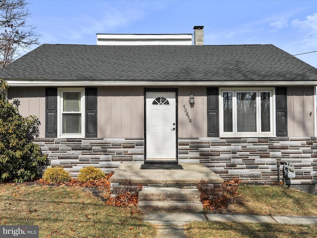 view of front of home featuring stone siding, a chimney, and roof with shingles