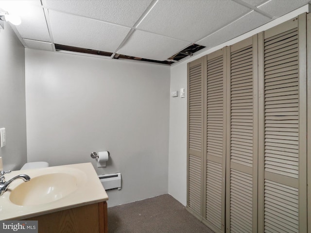 bathroom featuring a closet, baseboard heating, a drop ceiling, and vanity