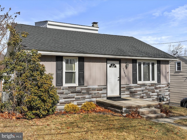 view of front of property with a shingled roof, stone siding, board and batten siding, a chimney, and a front yard