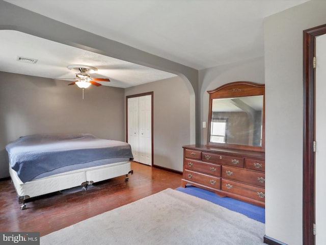 bedroom with arched walkways, dark wood-style flooring, a closet, visible vents, and a ceiling fan