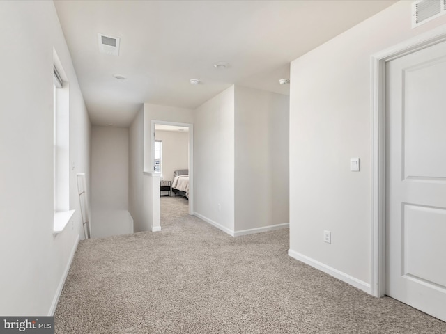 hallway with light carpet, visible vents, and baseboards