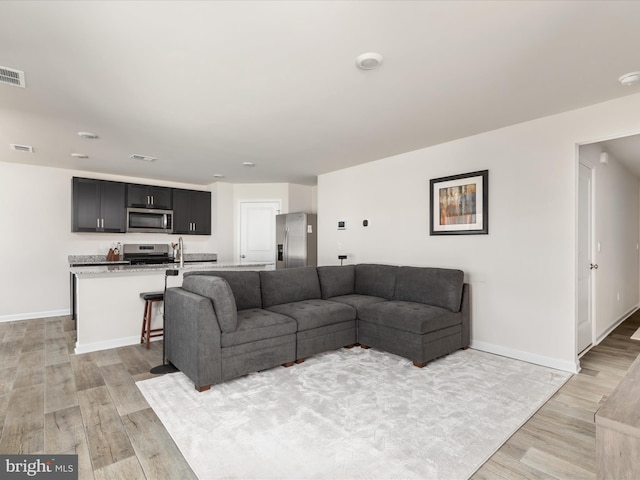 living area featuring light wood finished floors, visible vents, and baseboards