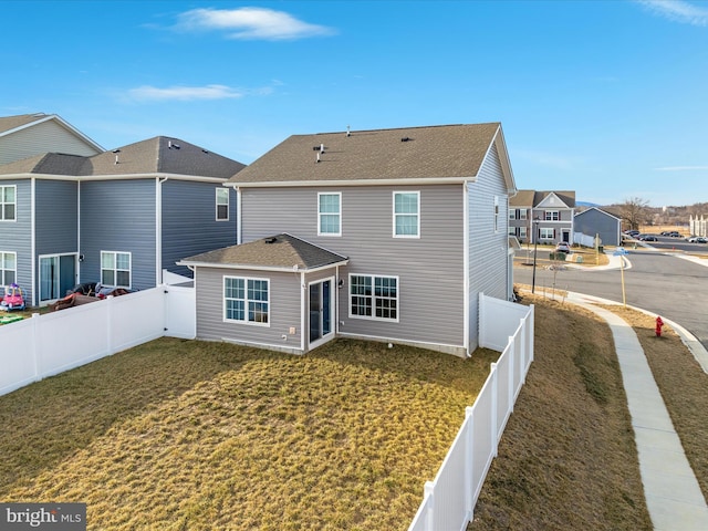 back of property featuring a shingled roof, a residential view, a fenced backyard, and a lawn