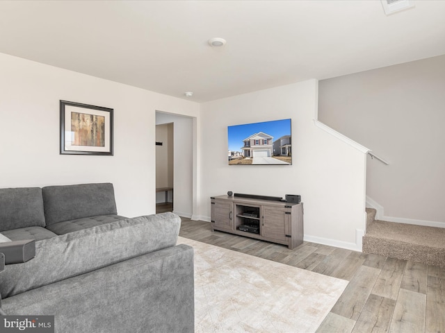 living room with light wood-type flooring, baseboards, and stairs