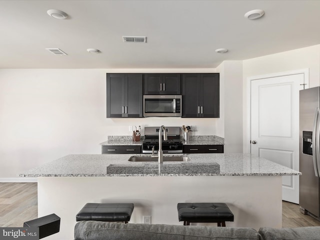 kitchen featuring a sink, light stone countertops, appliances with stainless steel finishes, and dark cabinets