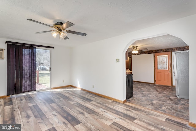 empty room with a textured ceiling, arched walkways, wood finished floors, a ceiling fan, and baseboards