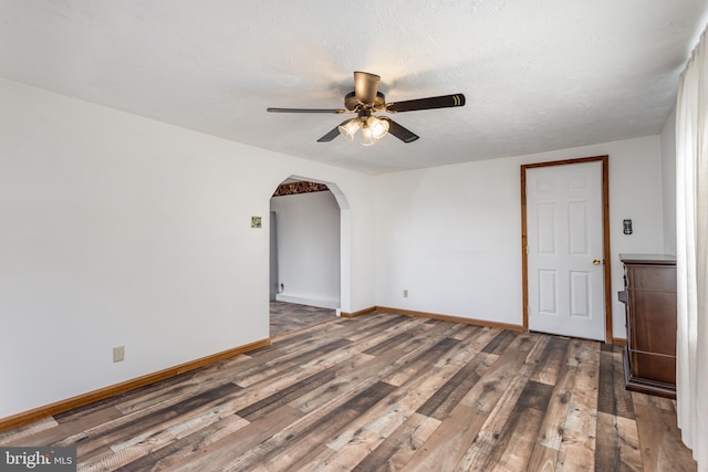 empty room featuring arched walkways, a textured ceiling, wood finished floors, a ceiling fan, and baseboards