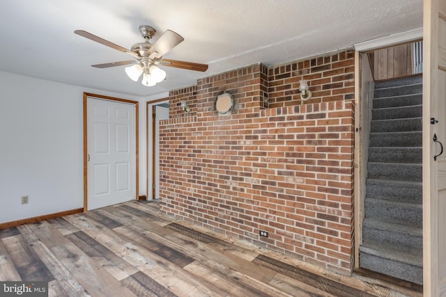 unfurnished room featuring baseboards, ceiling fan, stairway, wood finished floors, and a textured ceiling