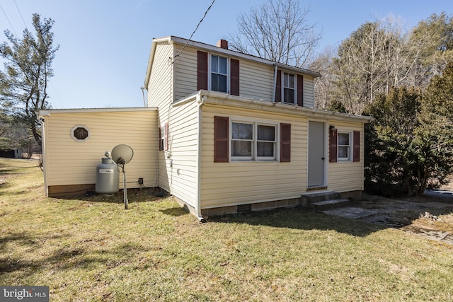 back of house featuring entry steps, a chimney, and a yard