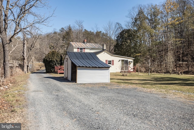 exterior space featuring gravel driveway, an outbuilding, metal roof, and a yard