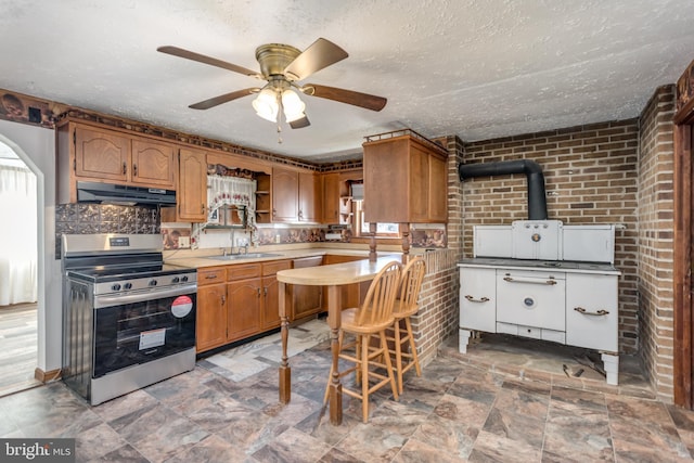 kitchen featuring a textured ceiling, under cabinet range hood, brick wall, electric range, and light countertops