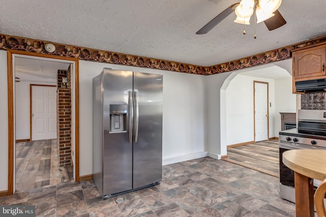 kitchen with under cabinet range hood, arched walkways, stainless steel appliances, and a textured ceiling