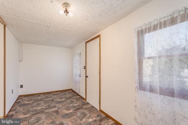 empty room with a textured ceiling, stone finish floor, and baseboards