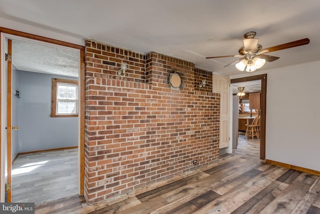 interior space with brick wall, a textured ceiling, baseboards, and wood finished floors