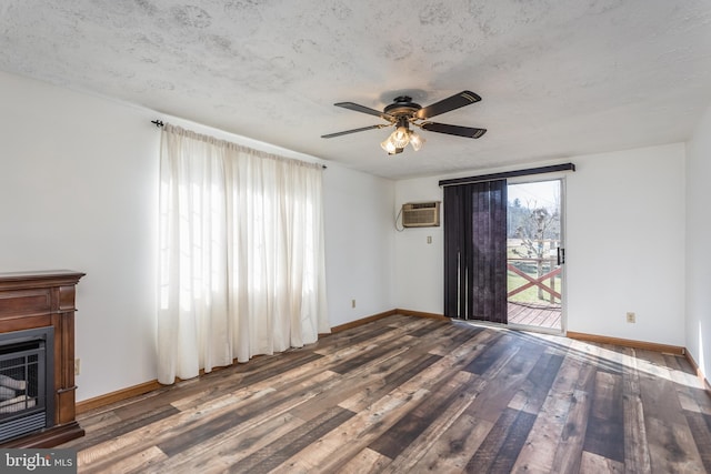 unfurnished living room with baseboards, wood finished floors, a textured ceiling, an AC wall unit, and a fireplace