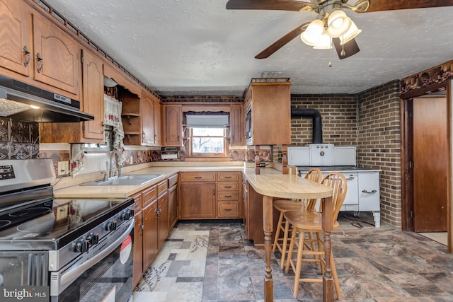 kitchen featuring brown cabinets, stainless steel appliances, light countertops, under cabinet range hood, and a sink