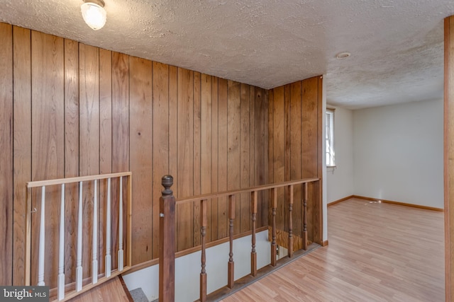 interior space featuring wood walls, a textured ceiling, baseboards, and wood finished floors