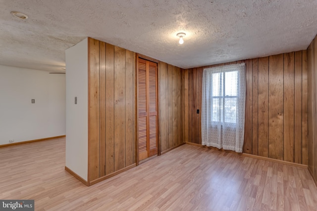 spare room with a textured ceiling, wood walls, wood finished floors, and baseboards